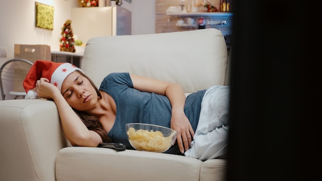 Adulto con cappello da Babbo Natale che dorme sul divano in televisione