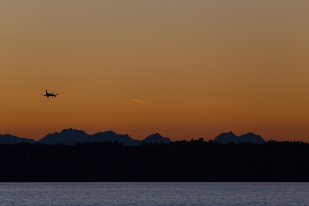 Aeroplano che sorvola le colline e il mare al tramonto