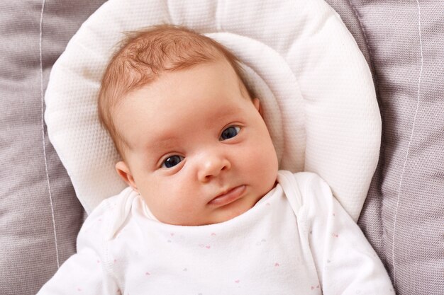 Affascinante adorabile bambino appena nato in una camicia bianca giace su una sedia a dondolo guardando la parte anteriore