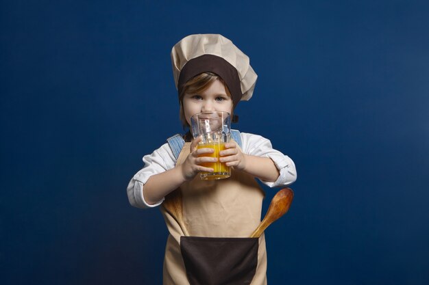 Affascinante bambina di 5 anni che indossa lo styling grembiule e cappello da cuoco in posa con utensili