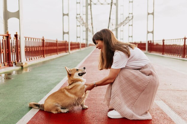 Affascinante bella ragazza in maglietta bianca e gonna sta giocando con il suo cane all'aperto