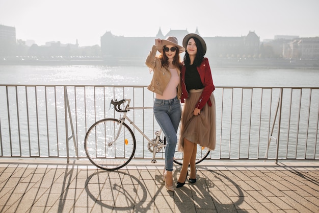 Affascinante donna castana in gonna in posa con l'amica in jeans