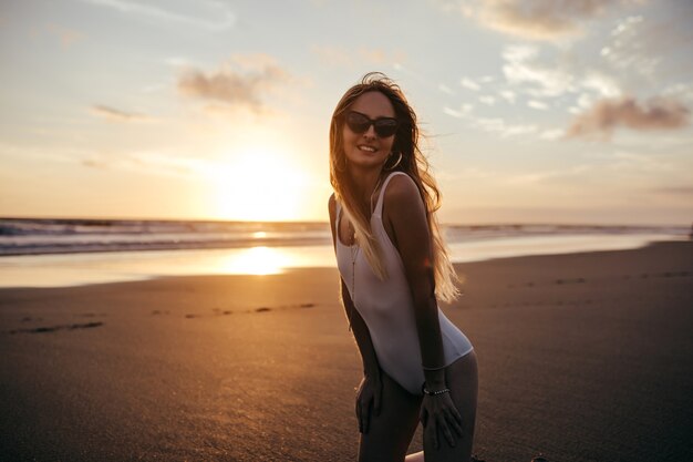 Affascinante donna caucasica in orecchini alla moda che propone alla spiaggia di sabbia in vacanza.