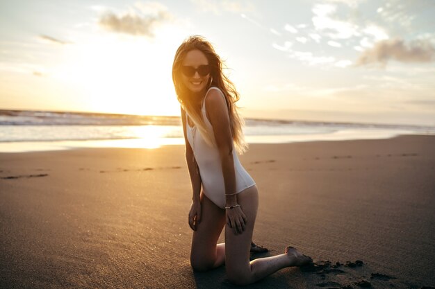 Affascinante donna caucasica in orecchini alla moda che propone alla spiaggia di sabbia in vacanza.