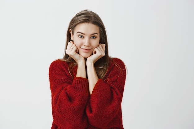 Affascinante donna europea corteggiamento con bei capelli biondi in maglione sciolto rosso, appoggiandosi la testa sulle mani e guardando con un sorriso carino positivo, ascoltando una storia interessante