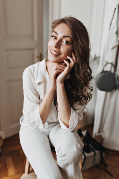 Affascinante donna in camicia bianca in posa in una stanza luminosa