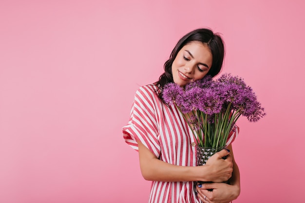 Affascinante donna italiana di buon umore posa con fiori viola.