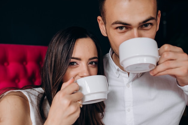 Affascinante giovane coppia di sposi beve caffè seduti su un divano rosa brillante