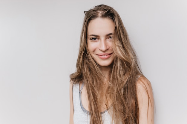 Affascinante giovane donna con un sorriso carino in posa. Foto dell'interno dell'adorabile modello femminile con lunghi capelli lucenti.