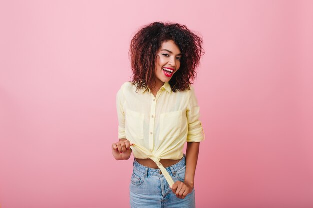 Affascinante giovane donna sottile con acconciatura africana in posa con piacere. Elegante ragazza di cattura in abbigliamento vintage agghiacciante.