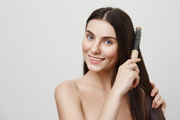 Affascinante giovane donna spazzolatura dei capelli e sorridente