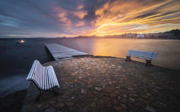 Affascinante paesaggio marino con un molo in legno e panchine in primo piano al tramonto panoramico