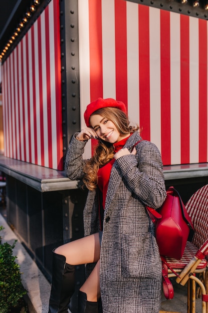 Affascinante ragazza in cappotto di tweed alla moda seduto per strada con un bel sorriso