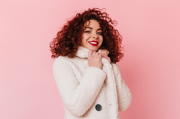 Affascinante signora vestita in camice bianco che guarda l'obbiettivo. Ritratto di ragazza dai capelli scuri con gli occhi azzurri in posa sullo spazio rosa.