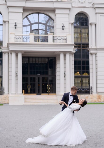 Affascinante uomo e donna che ballano per la prima volta all'aperto vicino al grande ristorante Coppia di sposi amorevoli che si godono il momento guardandosi Sposi e sposi carini che si divertono