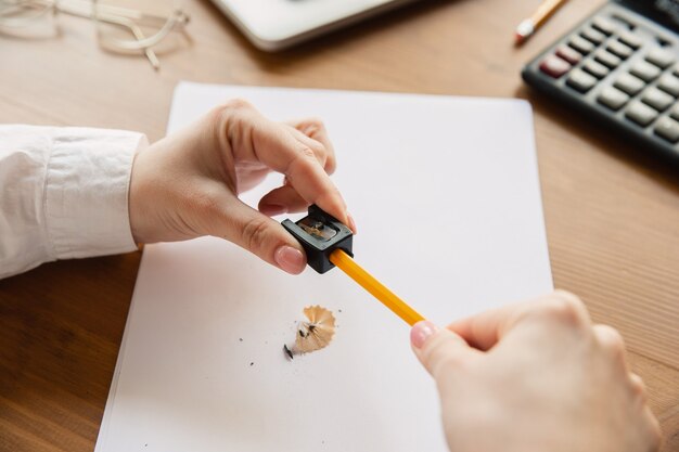 Affila una matita. Chiuda in su delle mani femminili caucasiche, lavorando in ufficio.