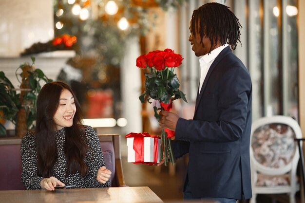 Africano in giacca e cravatta. La ragazza è felice. Bouquet di bellissimi fiori e un regalo