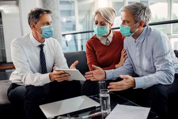 Agente assicurativo e coppia che indossano maschere facciali mentre utilizzano il touchpad in ufficio