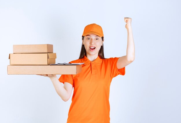 Agente di servizio femminile in uniforme di colore arancione che consegna più scatole di cartone e mostra il segno positivo della mano.