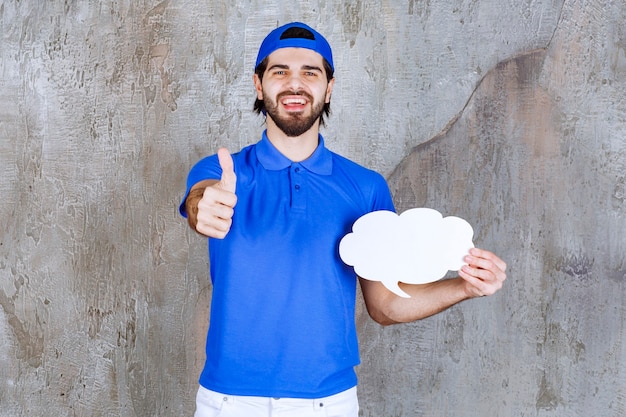 Agente di servizio maschio in uniforme blu che tiene una scheda informativa a forma di nuvola vuota e mostra un segno positivo con la mano.