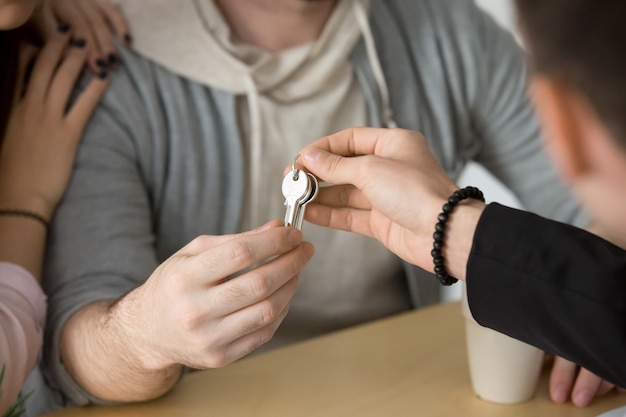 Agente immobiliare che fornisce le chiavi delle coppie, compranti il concetto della nuova casa, fine su