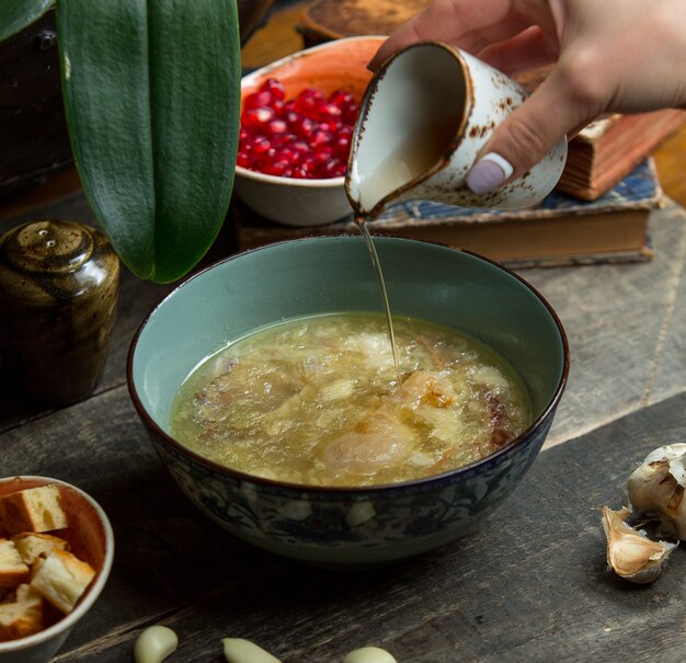 Aggiungendo brodo alla zuppa di pollo in una ciotola autentica blu