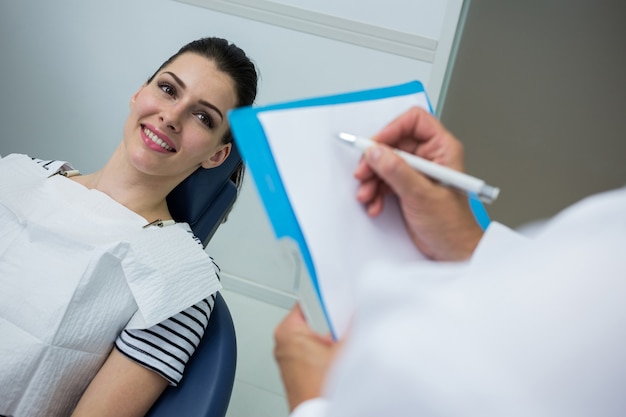 Aggiusti la scrittura sulla lavagna per appunti mentre paziente che si trova sul letto dentale