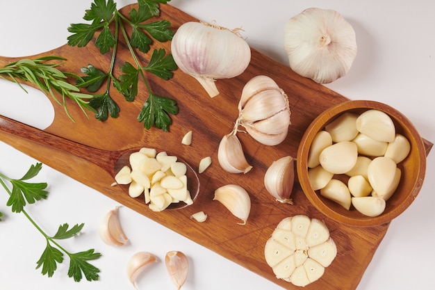 Aglio con rosmarino, prezzemolo e pepe in grani su una tavola di legno isolata su superficie bianca. Vista dall'alto. Lay piatto. appena raccolto dall'orto biologico di crescita domestica. Concetto di cibo.