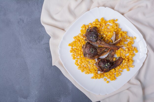 Agnello chomps sul piatto bianco con semi bolliti e tovaglia in raso sul blu.