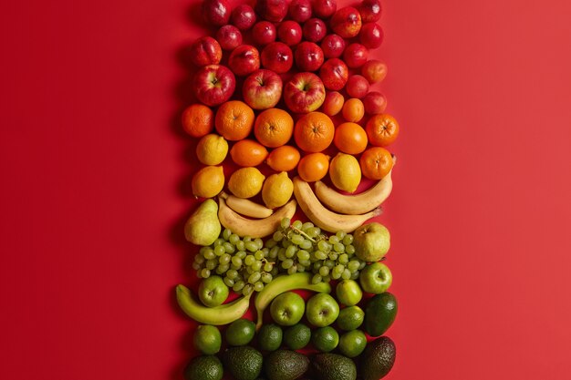 Agrumi sani assortiti su sfondo rosso brillante. Pesche mature, mele, arance, banane, uva e avocado per una sana alimentazione. Set di cibo nutriente. Dieta equilibrata, alimentazione pulita.