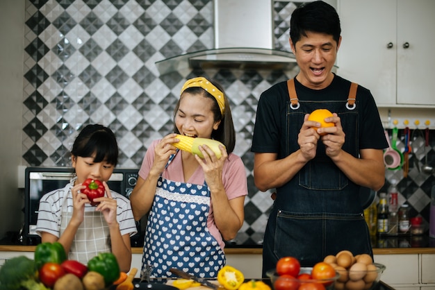 Aiuto sveglio della ragazza i suoi genitori stanno tagliando le verdure e stanno sorridendo mentre cucinano insieme nella cucina