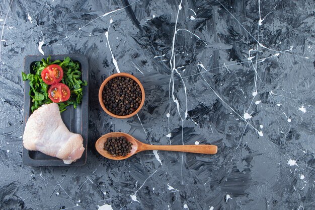 Ala di pollo e verdura su una tavola accanto alla ciotola delle spezie e al cucchiaio, sullo sfondo di marmo.