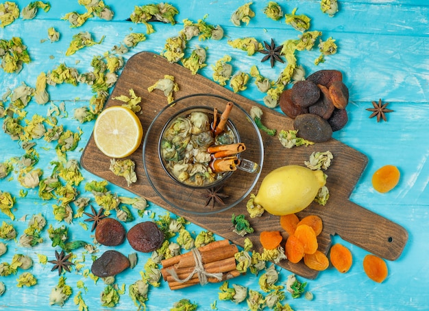 Albicocche secche con spezie, tè, limone, erbe aromatiche su blu e tagliere.