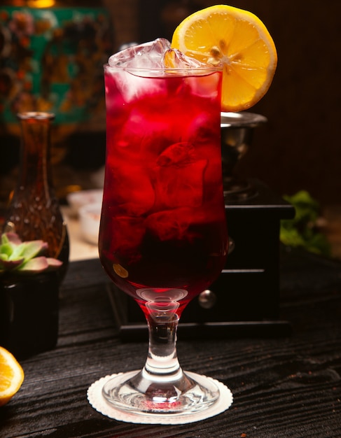 Alcool rosso cocktail in vetro con cubetti di ghiaccio e fetta di limone