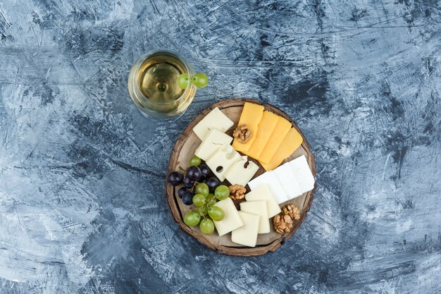 Alcune uve con un bicchiere di vino, formaggio, noci su intonaco e sfondo di legno, vista dall'alto.