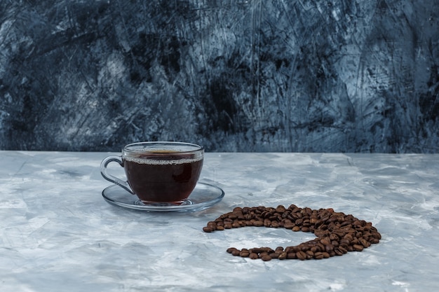 Alcuni chicchi di caffè con la tazza di caffè su fondo di marmo blu scuro e chiaro, primo piano.