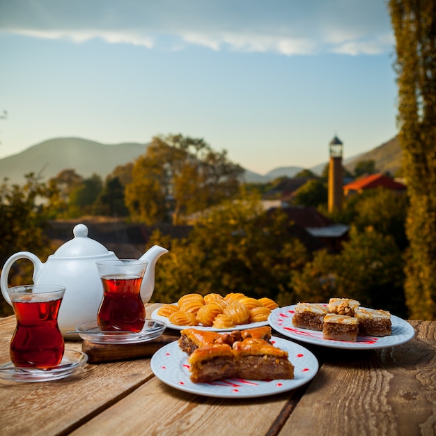 Alcuni dessert turchi con bicchieri di tè e teiera su un tavolo con il villaggio sullo sfondo, vista laterale.