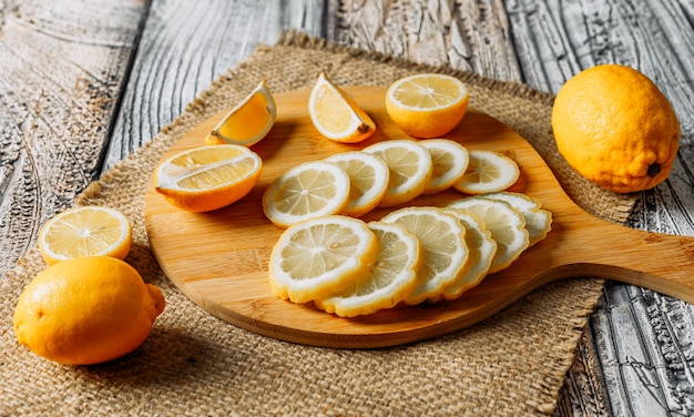 Alcuni limoni con le fette sul tagliere, sul panno e sul fondo scuro, vista dell'angolo alto.