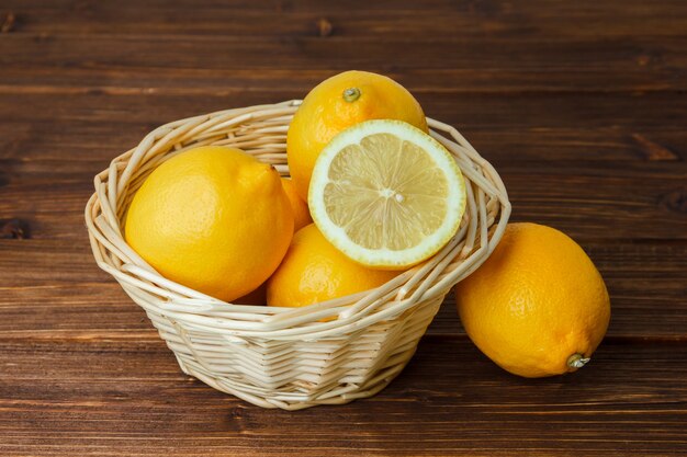 Alcuni limoni gialli con fette di limone in un cesto su una superficie di legno, ad alto angolo di visione.