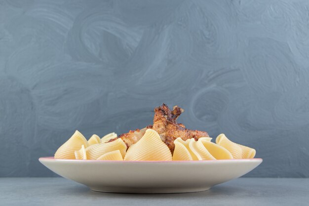 Ali alla griglia e pasta di conchiglie sul piatto rosa.