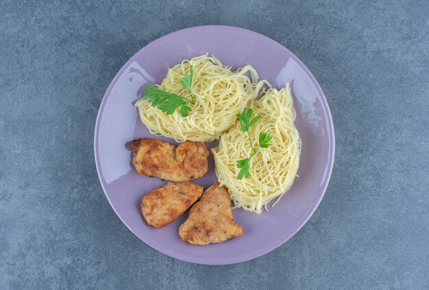 Ali di pollo alla griglia e spaghetti sul piatto viola.