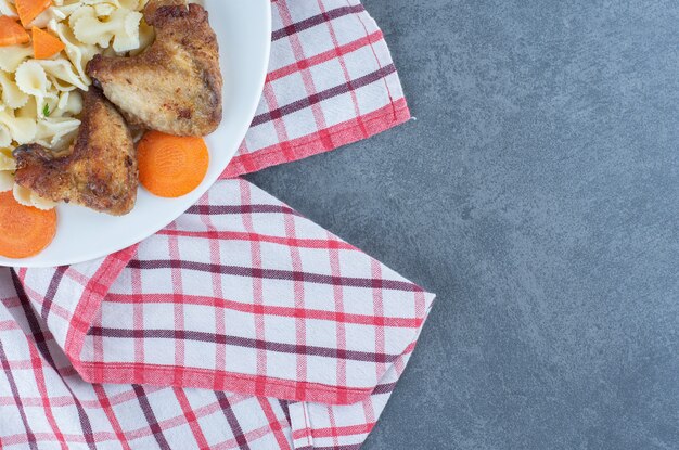 Ali di pollo arrosto e pasta sul piatto bianco.