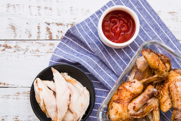 Ali di pollo bollite e arrosto con salsa di pomodoro sul tovagliolo blu contro tavolo in legno
