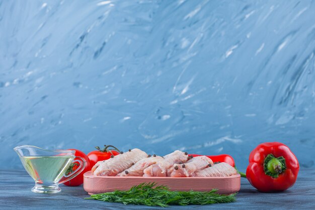 Ali di pollo in un piatto di legno accanto a pomodori e pepe, su sfondo blu.