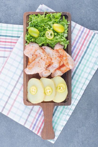 Ali di pollo marinate e verdure su tavola di legno.