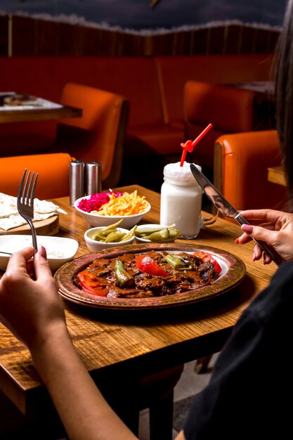 Alla donna viene servito il kebab di iskender in un piatto di rame con yogurt sottaceto e ayran