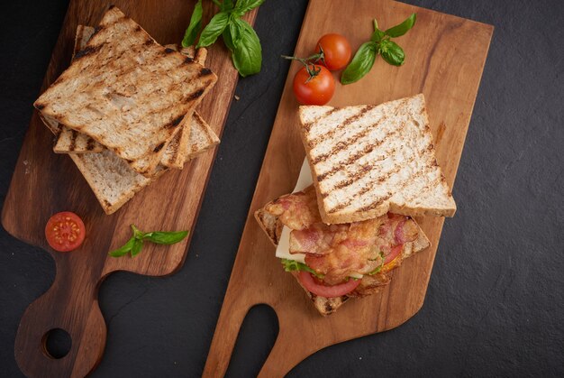 Alla griglia e panino con pancetta, uovo fritto, pomodoro e lattuga serviti sul tagliere di legno