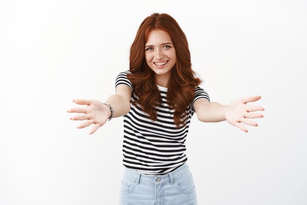 Allegra donna rossa in maglietta a righe magra in avanti estendere le braccia vuole tenere o avere qualcosa tra le braccia sorridendo gioiosamente abbracciando amico saluto con abbracci accoglienti sfondo bianco