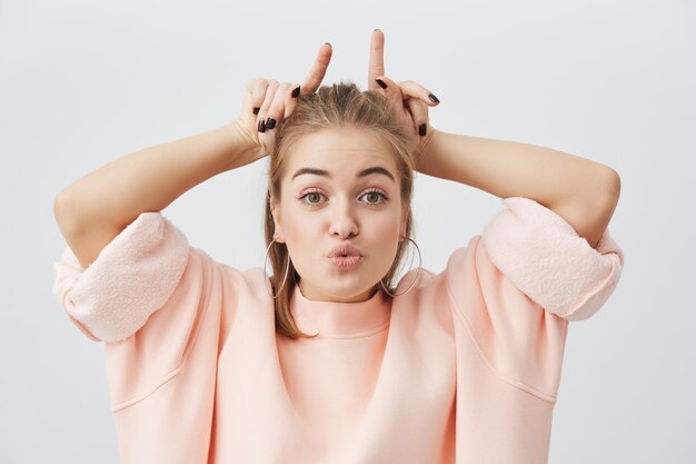 Allegra giocosa bella femmina caucasica essendo felice, divertendosi, beffardo con gli amici, mostrando il dito indice sopra la sua testa. Persone ed emozioni positive.