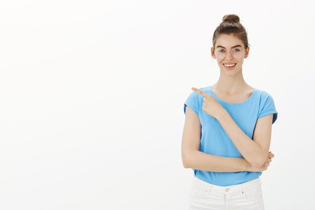 Allegra giovane donna sorridente, mostrando il modo, puntando il dito a sinistra in pubblicità